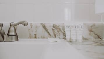 Un baño con lavamanos de mármol, un grifo y tres botellas de champú y acondicionador.