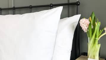 A neatly made bed with white linens, a black headboard, and a bedside table with a vase of flowers and a thank you card.
