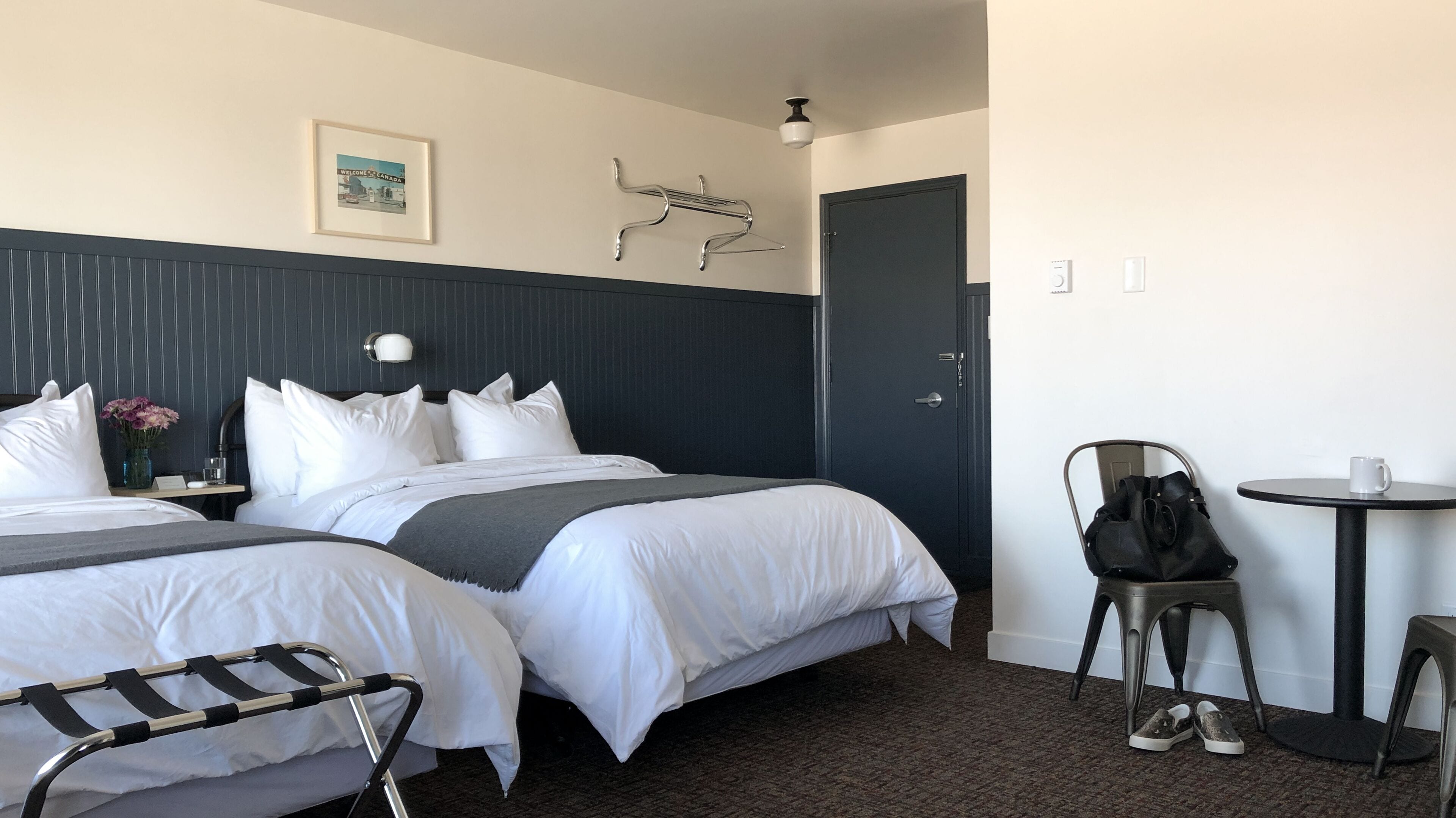 Una habitación de hotel con dos camas, una mesita, una silla y una puerta.