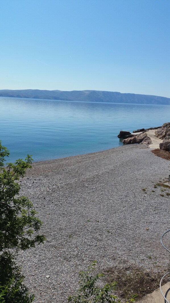 Experience the serene tranquility of a natural beach setting with a pebble-strewn shoreline and breathtaking views of distant hills.
