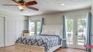 Un dormitori amb un llit, un ventilador de sostre, una finestra amb cortines i vista a l'exterior.