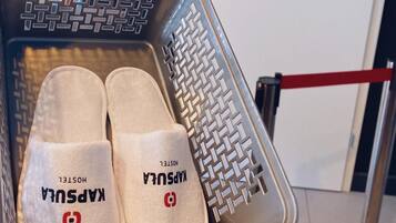 A metal cart with two pairs of slippers labeled "Kapsula" and "Hostel" in a hotel setting.