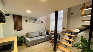 A modern interior with a staircase, wooden tables, a grey sofa, and a plant. - Kapsuła Hostel Warszawa (Warsaw)