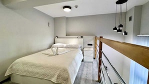 A modern hotel room with a large bed, a bedside table, a small bedside cabinet, and a wooden railing. - Kapsuła Hostel Warszawa (Warsaw)