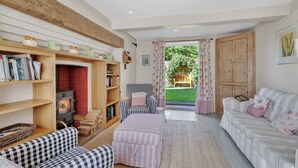 A cozy living room with a fireplace, checkered furniture, and a view of a garden through a glass door. - Church Cottage - sleeps 6 guests  in 3 bedrooms (Burford)
