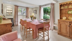 A dining area with a checkered tablecloth, wooden chairs, and a buffet cabinet. - Church Cottage - sleeps 6 guests  in 3 bedrooms (Burford)