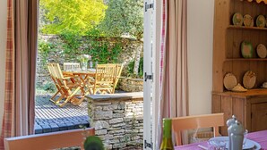 An open doorway leading to an outdoor patio with a stone wall, wooden furniture, and a shelf with decorative plates. - Church Cottage - sleeps 6 guests  in 3 bedrooms (Burford)