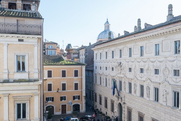A narrow street with historic buildings, including a building with a dome and another with classical architecture.