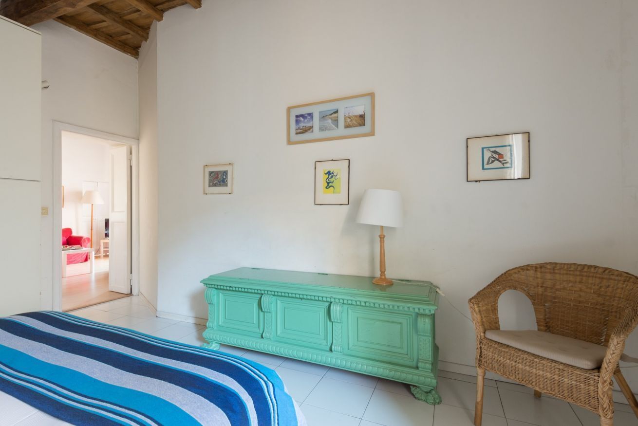 Um quarto com uma cama, uma cômoda verde, uma cadeira de vime e quadros nas paredes.