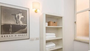 A bathroom with a framed black-and-white photo, a white shelf with towels, and a wall-mounted light fixture. - Navona Charming Terrace Apartment (Rome)