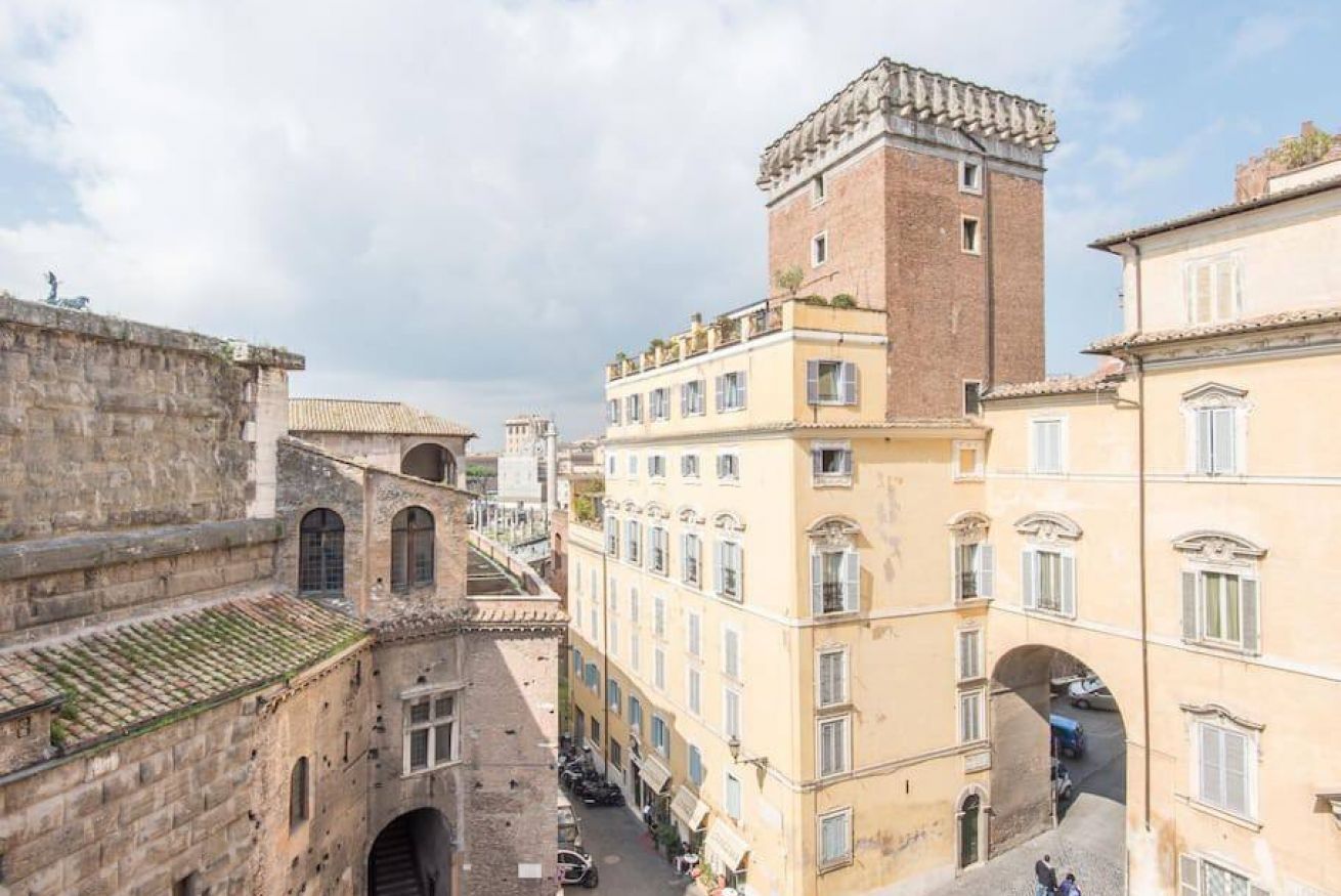 A narrow street with historic buildings, including a tower and a building with a balcony.