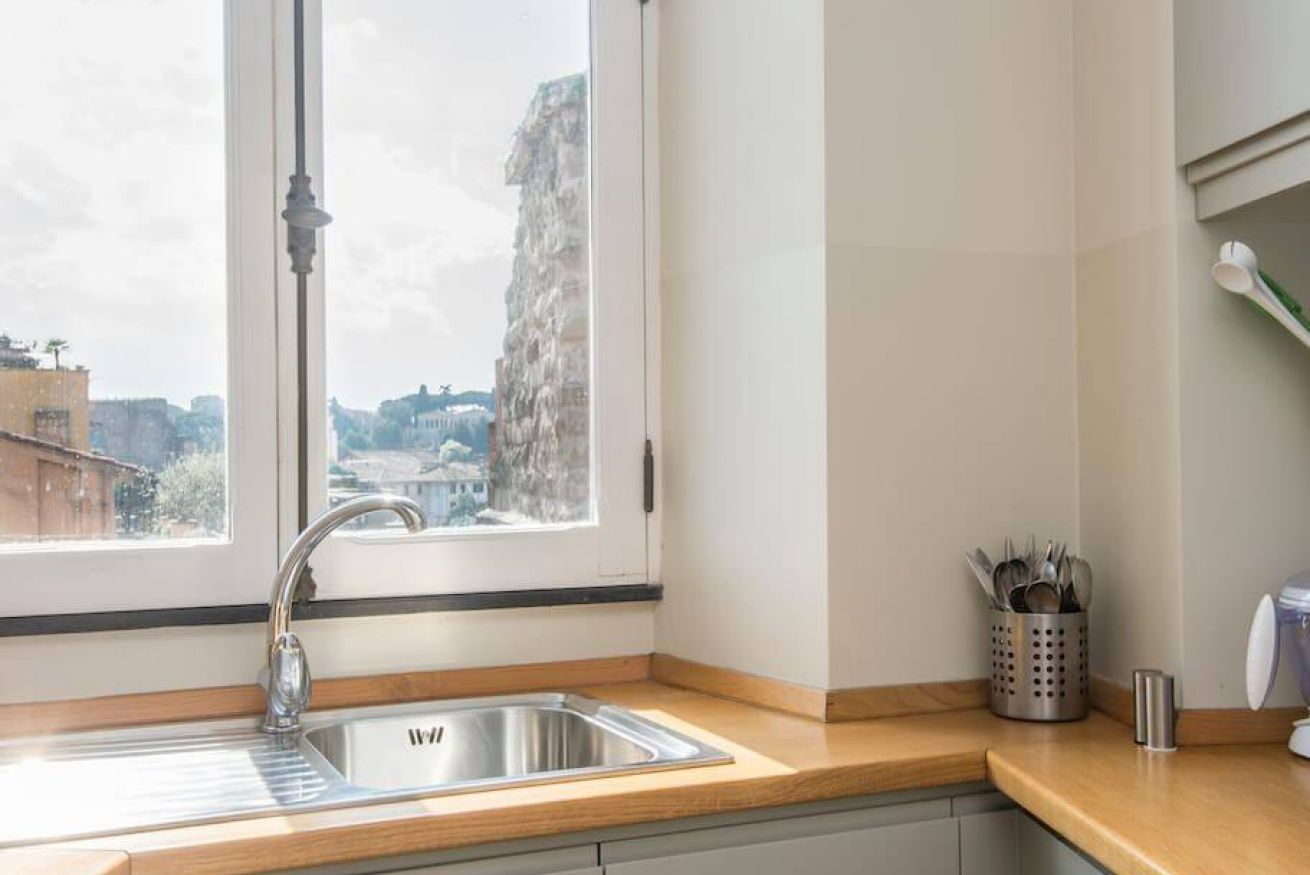 A kitchen with a window, a stainless steel sink, and a utensil holder.