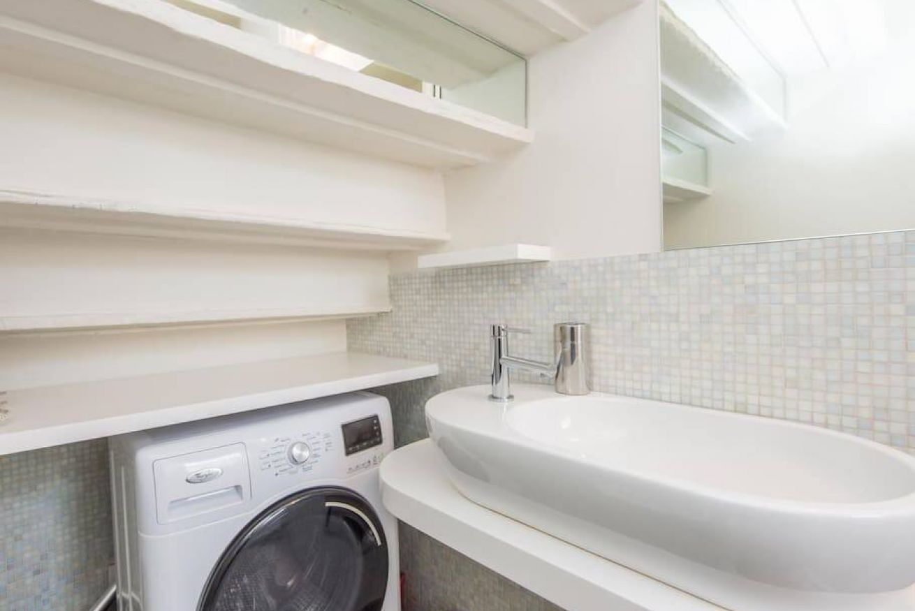 A bathroom with a washing machine, a sink, and a tiled backsplash.