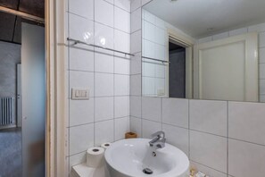 Ein Badezimmer mit weißen Fliesen, einem Waschbecken, einem Spiegel und einem Handtuchhalter.