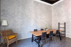 A conference room with a wooden table, black chairs, a wicker chair with a yellow cushion, a floor lamp, and a metal shelf unit.
