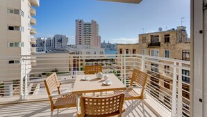 A balcony with a table and chairs, overlooking a cityscape with buildings and a clear sky. - Fabulous Apartment with Pool, Upmarket Area (Sliema)