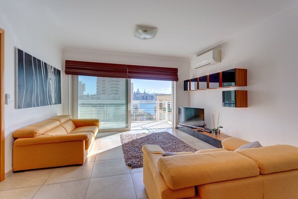 Una sala de estar moderna con un conjunto de sofás, un televisor de pantalla plana y un ventanal con vistas a la ciudad.