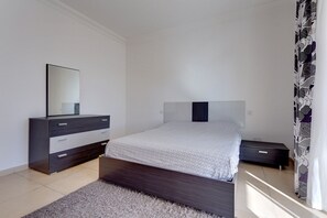 Un dormitorio con cama, cómoda, espejo y ventana con cortinas.