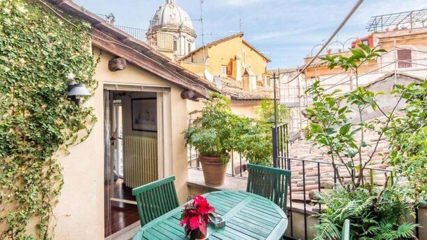 A courtyard with a table and chairs, a potted plant, and a building with a dome in the background. - Campo de Fiori Luxury House (Rome)