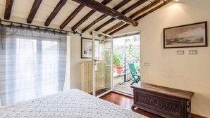 A bedroom with a bed, wooden ceiling beams, a radiator, a green chair, and a wooden cabinet. - Campo de Fiori Luxury House (Rome)