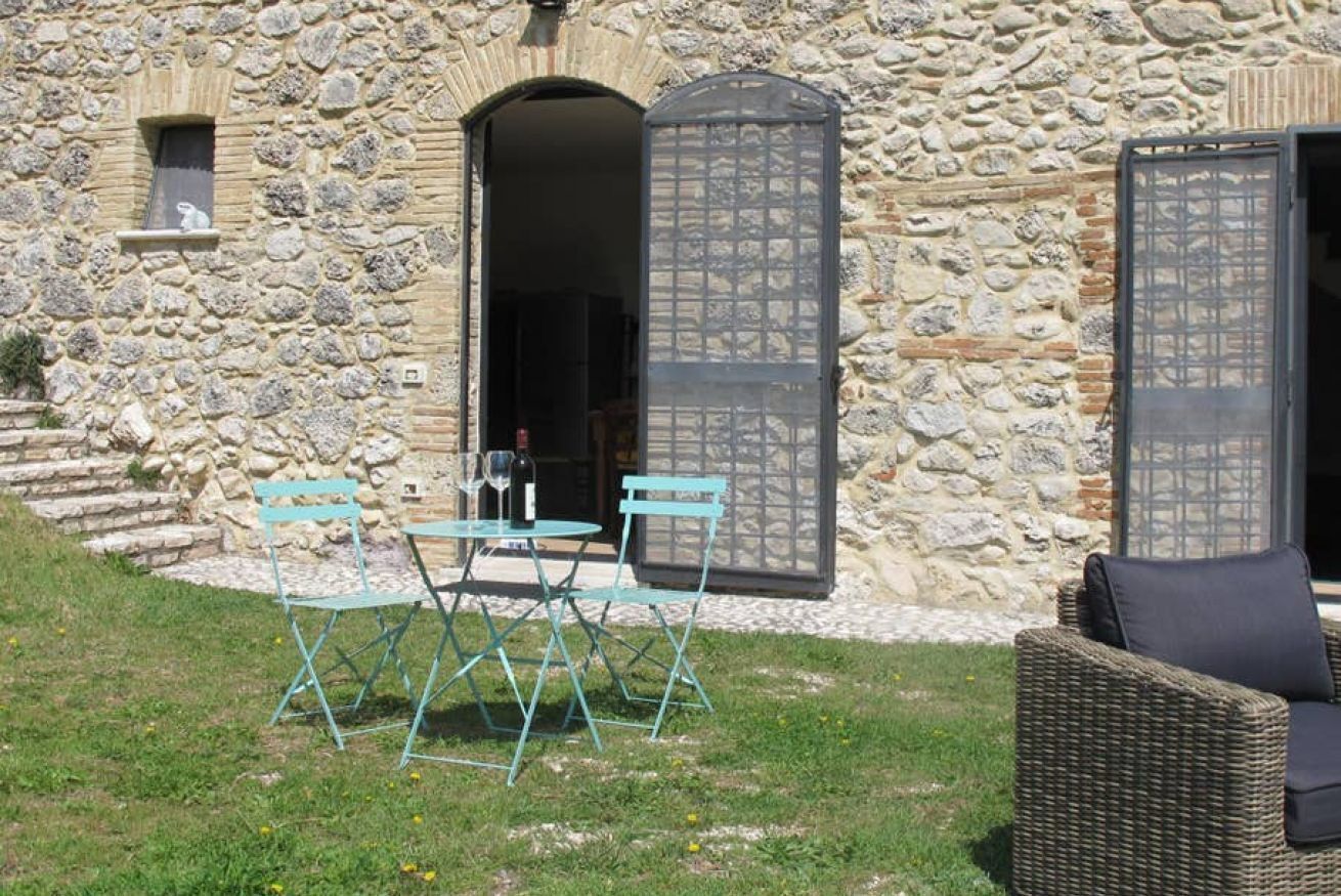 Edificio de piedra con un patio que cuenta con una mesa, sillas, una silla de mimbre y una pequeña estatua.