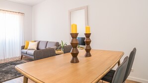 A dining area with a wooden table, two candles, and a grey sofa with yellow cushions. - Binge Green Apartment, Wifi, AC (Faro)