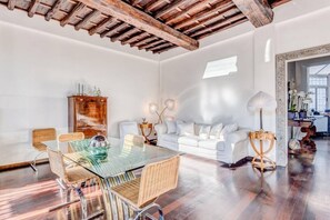 A spacious room with a glass dining table, wicker chairs, a white sofa, and a wooden ceiling.