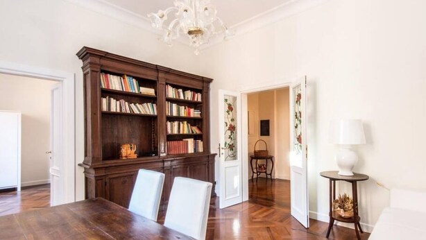 Un comedor con mesa y sillas de madera, una estantería y una araña.