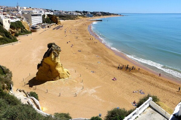 A coastal beach with a prominent cliff, sandy shore, and buildings in the background. - Binge Red Apartment, Wifi, AC, Terrace (Faro)