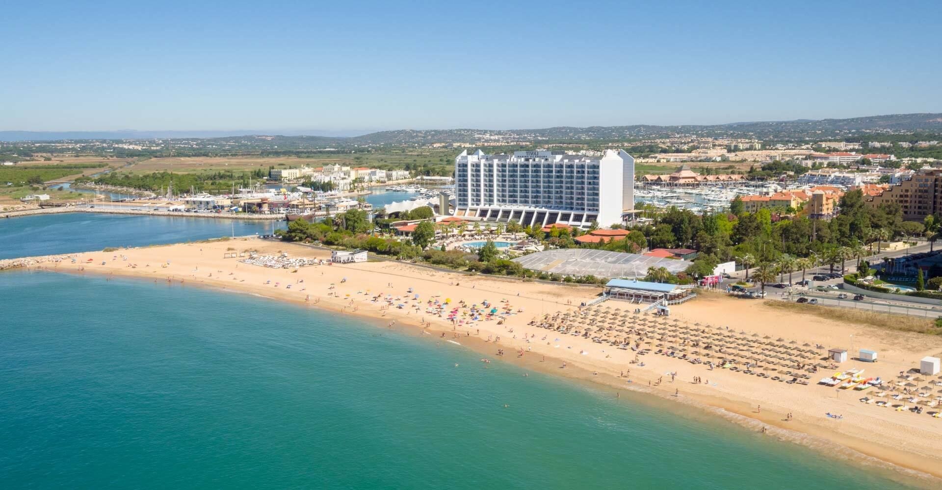 Un hôtel en bord de mer offrant une vue sur la plage, plusieurs piscines et un port de plaisance.