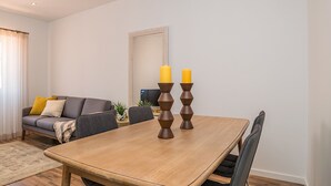 Una sala de estar moderna con una mesa de comedor de madera, un sofá con cojines y un televisor.