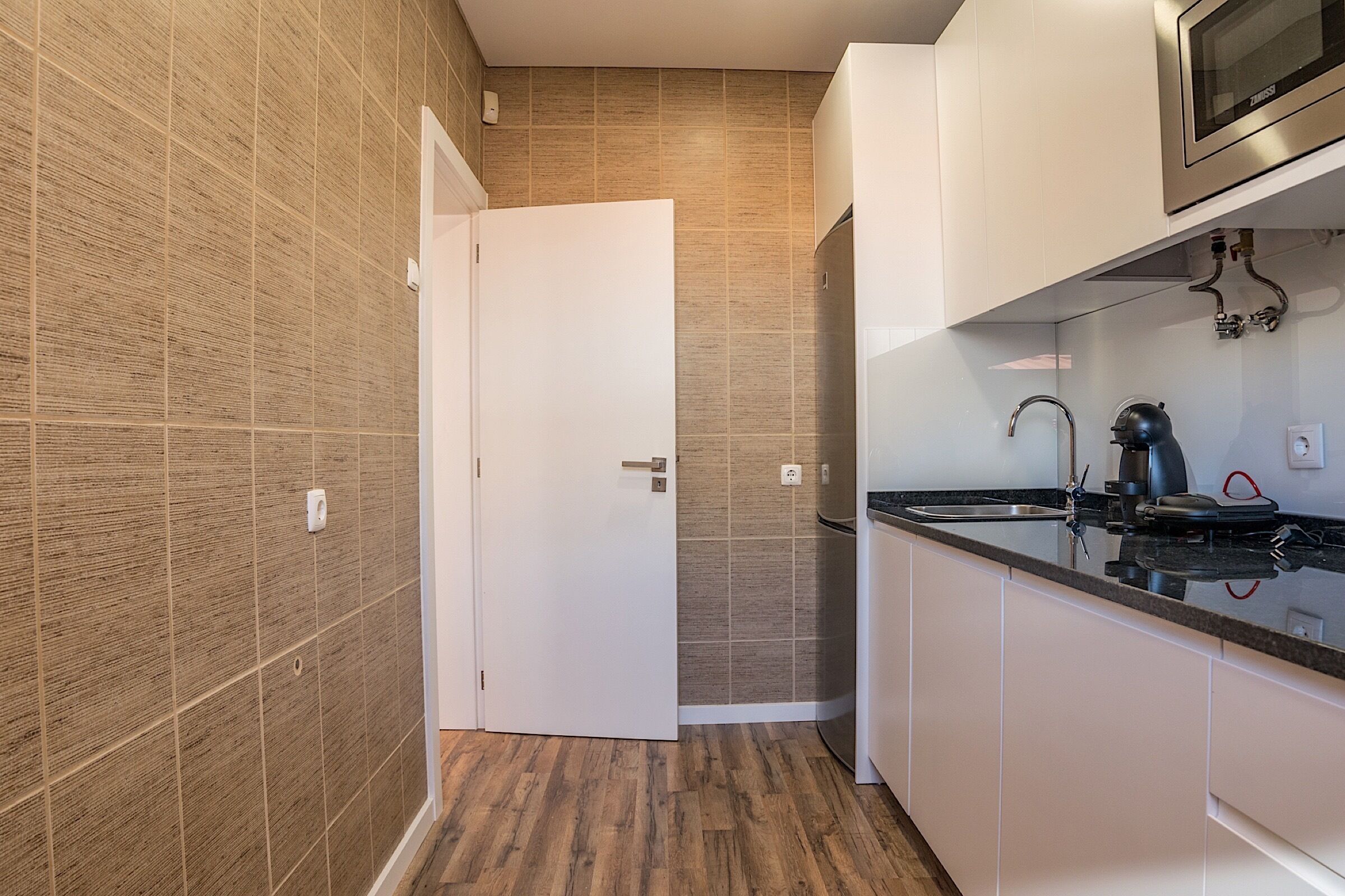 Een moderne keuken met witte kasten, een RVS magnetron en een houten vloer.