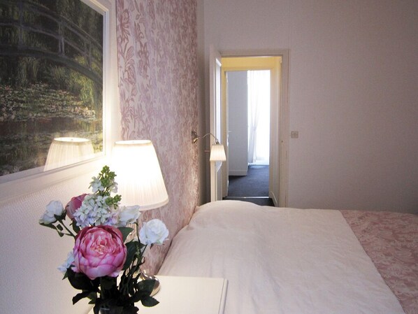 Una habitación de hotel con una cama, una mesita de noche con una lámpara y un jarrón con flores.