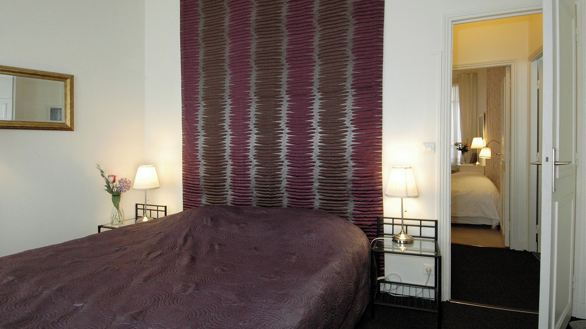 A hotel room with a large bed, two bedside tables with lamps, a mirror, and a patterned curtain.