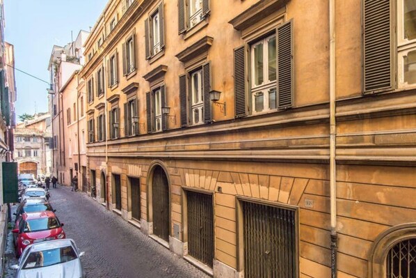 A narrow cobblestone street lined with historic buildings, featuring arched windows and shutters.