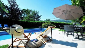 Een zwembadterras met ligbedden, een tafel en een parasol.