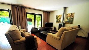 Een woonkamer met twee banken, een flatscreen televisie, een open haard en een groot raam met gordijnen.