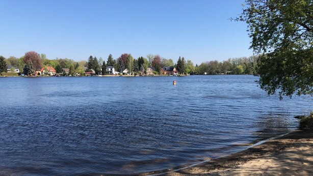 Une vue sur le lac, avec une plage de sable, une eau calme et des maisons en arrière-plan.