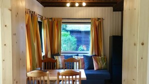 Un intérieur chaleureux avec une table et des chaises en bois, un canapé avec des coussins et une fenêtre agrémentée de rideaux.