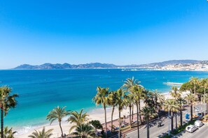 Blick auf die Küste mit Strand, Palmen und einer entfernten Stadtlandschaft.