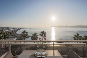 A balcony with a table, a vase with flowers, and a view of the sea and mountains.