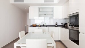 Een moderne keuken met witte kastjes, een eettafel met glazen blad en ingebouwde apparatuur.
