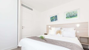 Een slaapkamer met een bed, nachtkastje, deur en twee aan de muur hangende schilderijen.