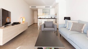 Een moderne woonkamer met een flatscreen-tv, een salontafel, een bank en een eethoek op de achtergrond.