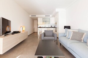 A modern living room with a flat-screen TV, a coffee table, a sofa, and a dining area in the background.