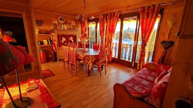 L’intérieur chaleureux d’un chalet en bois comprend un coin repas, un canapé et offre une vue sur un paysage montagneux grâce à de grandes fenêtres.