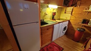 Une cuisine de taille réduite, équipée d’un réfrigérateur, d’un lave-linge et de meubles de rangement en bois.
