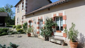 A building with a tiled roof and brick accents, surrounded by gravel and potted plants. - Charming cottage in the country of Futuroscope (Persac)
