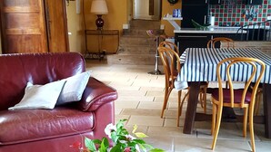A living room with a leather sofa, a dining table with chairs, a wooden coffee table with a vase of flowers, and a kitchen in the background. - Charming cottage in the country of Futuroscope (Persac)