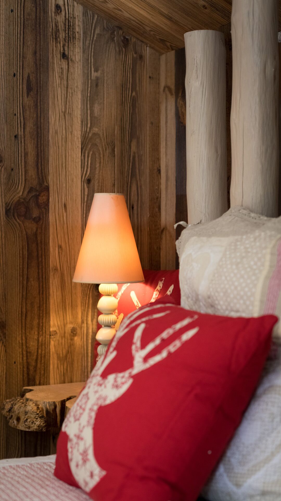 A wooden cabin interior with a bed, a red pillow, and a lamp.